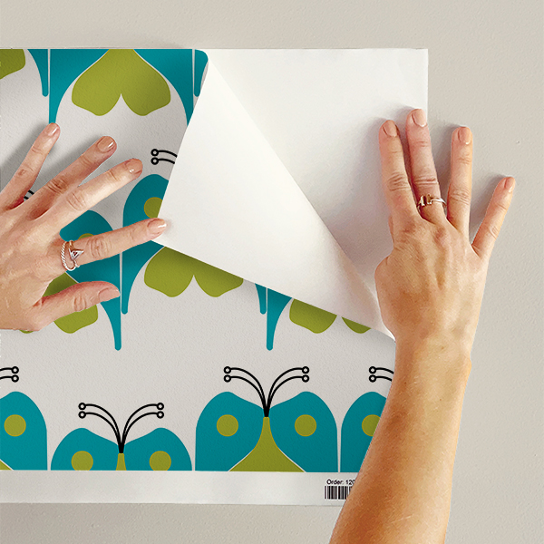 The artwork features a repeating geometric pattern of symmetrical shapes resembling elongated, curved diamonds or petals in various shades of blue and green. Each shape is split vertically with one half filled with a light blue and the other half filled with green or darker blue. The background is a light, almost pastel blue, which provides a soft yet vibrant backdrop. One of the blue shapes near the upper left contains a white starburst element, adding a focal point of brightness to the composition. The overall design conveys a modern, mid-century aesthetic with clean lines and harmonious color contrasts.